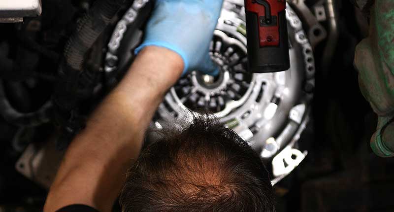 close up center view photo of an mt gear clutch specialists hands replacing a ford clutch system with the clutch pressureplate in place being bolted to the cars flywheel