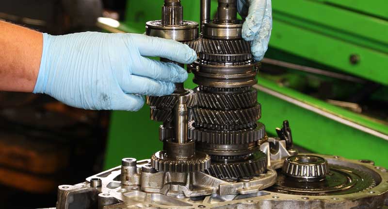 close up photo of an mt gear specialists hands wearing blue plastic gloves in sheffield reconditioning a ford gearbox partially dismantled on its side showing shiny metal gears on two seperate shafts