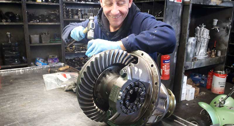 close up side view photo of an mt gear differentials specialist reconditioning a audi faulty car differential that is fully dismantled on a metal bench with two very large shiny metals gears visible